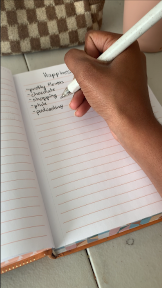 Close-up of a hand writing in a journal with a glass of water and pencil case on a desk as part of a realistic summer routine.